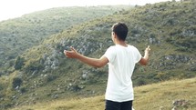 young man standing outdoors with outstretched arms worshiping 