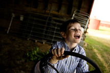 happy boy child with his hands on a tractor steering wheel 