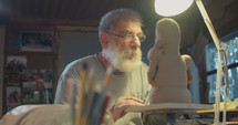 Old sculptor working on a clay sculpture in his small studio