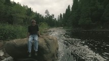 a man sitting on a rock along a river 