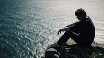 man sitting on a rock looking out onto the ocean 