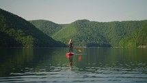 woman riding a paddle board on beautiful lake with tree covered mountain peaks