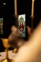 Out of focus shot of a communion wafer being broken with a stained glass window of Jesus in the background.