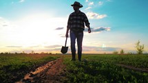 Agriculture concept. Silhouette of a man with a shovel. A tired peasant walks across the field after hard work. Worker agronomist with a shovel goes to sunset. Work on agricultural land concept.