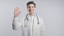 Friendly American Mature 30s physician man in white medical coat form waving Hand - Hello, Hi. Greetings on white studio. High quality 4k footage