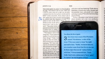 cellphone opened to a Bible app and an open Bible 