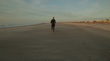 man running on a beach and stopping to look at a shell 