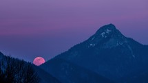 Red full moon is rising over mountain forest in winter evening nature Time lapse