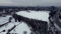 Aerial push-in shot of Riverdale Park East in dynamic urban Toronto on a cold winter day. Aircraft flying right above a bunch of trees while a group of people are playing with snow in the distance. 