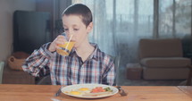 Young boy drinking orange juice for breakfast.