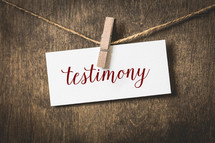 word testimony on white card stock hanging from a clothespin on a clothesline 