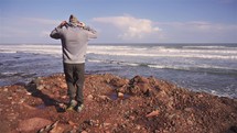 Man walk on the rocky beach and looks out over ocean water waves in summer holiday
