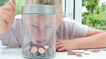 Caucasian girl putting coins in to a money jar