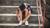 boy sitting on steps tying his shoes 