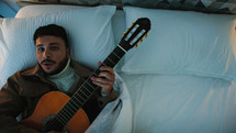 Man singing and playing the guitar in a bed