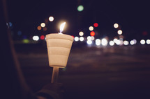 A man standing on a street corner holding a candle 