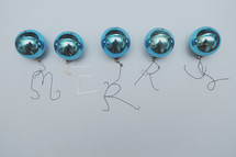 A row of vintage blue Christmas ornaments with the word "merry" written with string.