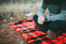 man sitting and praying on a plaid blanket outdoors 