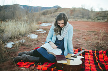 woman sitting on a plaid blanket with her guitar reading 