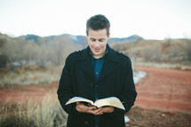 man standing outdoors reading a Bible 