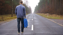 a man with a suitcase standing in the middle of a road 