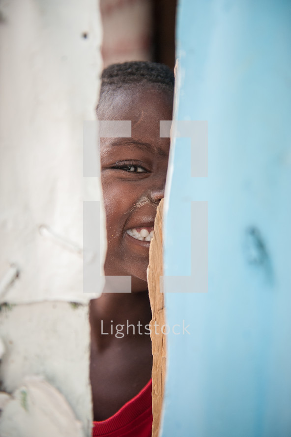 a smiling child peeking through a crack 