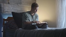 a young man reading a Bible sitting in bed 