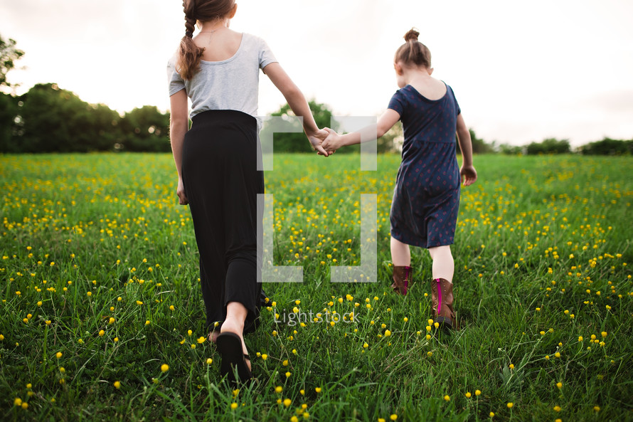 sisters walking in a meadow of yellow wildflowers holding hands 