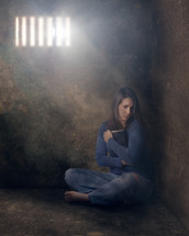 a woman sitting alone in a cell grasping a Bible 