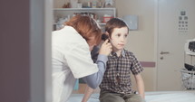 Female doctor examining a young boy's ear canal using an otoscope in the clinic.