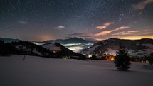 Starry night sky with stars and colorful clouds moving fast over winter mountains in rural landscape time lapse
