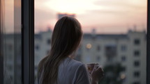 Young girl on the balcony watching the sunset and drinking tea. Middle shot