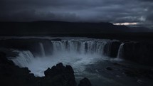 Wide cascading waterfall in Iceland at night with scenic clouds and mountains in the background