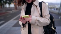 Young woman using smartphone on city street. Close-up female hands surfing internet with mobile device. Autumn season. Technology, social apps, connection concept. High quality 4k footage