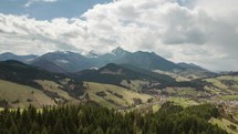 Aerial flight over spring landscape with clouds moving over mountains time lapse. Pan left to right
