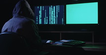 Computer hacker sitting in a dark room hacking security systems