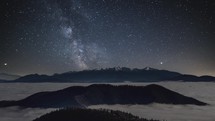 Milky way galaxy in starry night sky over snowy winter alps mountains above foggy clouds landscape Astronomy Time lapse
