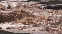 Slow motion of muddy river rapids with water splashing after heavy storm