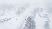 Drone flying down a snow covered neighborhood street during a snow storm.