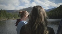 young people standing at the edge of a lake looking at mountains 