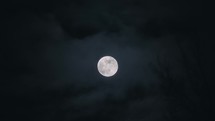 Full moon glowing in the night sky full of misty atmospheric clouds