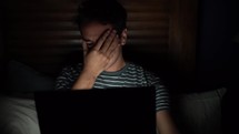a man looking at a computer screen alone in a dark room 