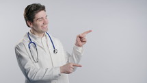 Smiling mature physician man in white medical coat form looking to empty place for your advertising. Recommending medical specialist pointing at right side, copy space. Successful presenting. High 4k