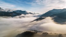 Aerial view of clouds rolling over mountains at sunrise.