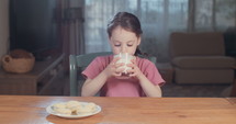 Little girl drinking milk sitting at home.