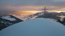 Aerial view of Religious Christian steel cross on snowy hill in winter nature landscape at sunrise
