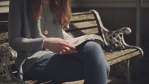 woman reading a Bible outdoors on a park bench 