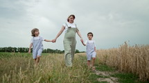 Young family - pregnant mom and two brothers twins boys walking on green path near wheat field, farmland. Happy mother and children, love, freedom, future, home, countryside, green childhood