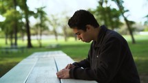 a man sitting at a picnic table reading a Bible 