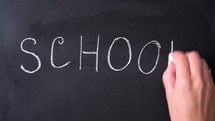 Bold white chalk letters spell School. Inscription SCHOOL. Chalk writing on blackboard. Concept of beginning of school year.	